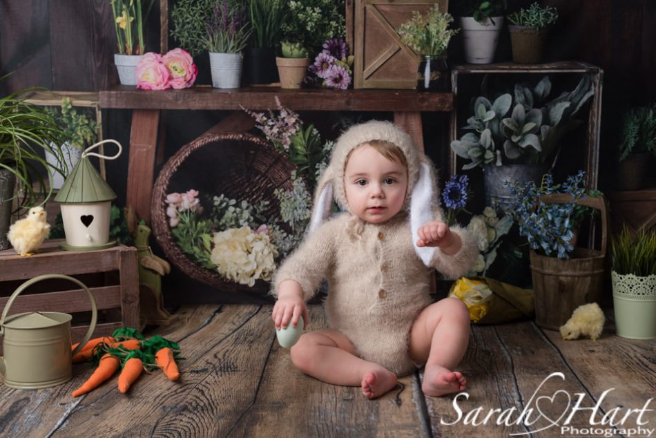 Baby dressed in bunny outfit on a dark wooden backdrop with Spring flowers at Spring Photography Mini Session
